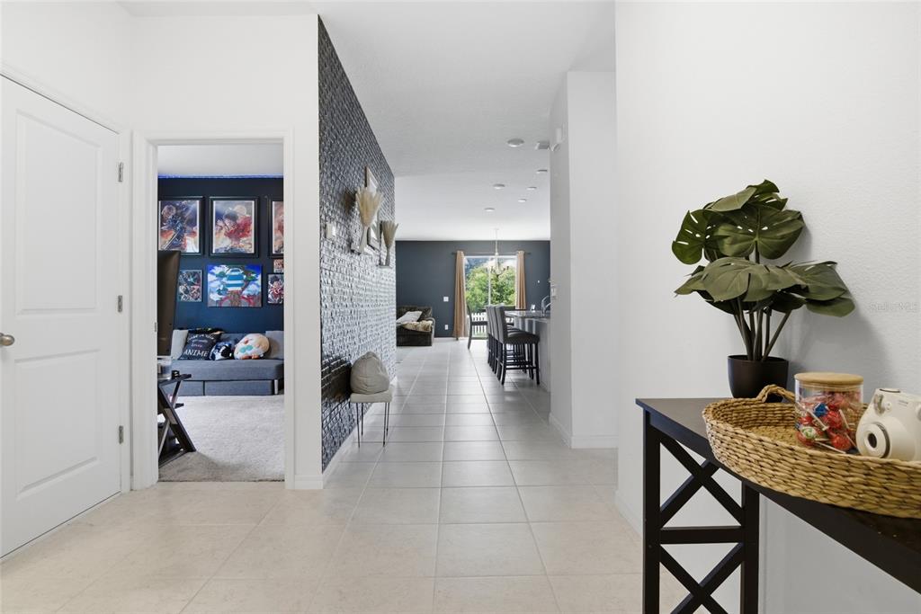 A hallway with tile flooring leads to an open kitchen and a room with wall art — 2004 BUCKHANON TRL, DELAND, FL