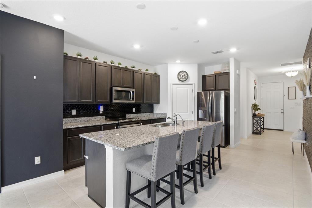 A kitchen features dark wood cabinets, granite countertops, a central island, and gray bar stools — 2004 BUCKHANON TRL, DELAND, FL