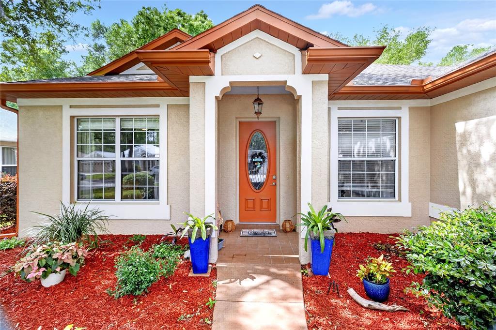 The exterior of a single-story home features a tan stucco facade, orange door, and red mulch — 19562 SW 84TH PLACE, DUNNELLON, FL