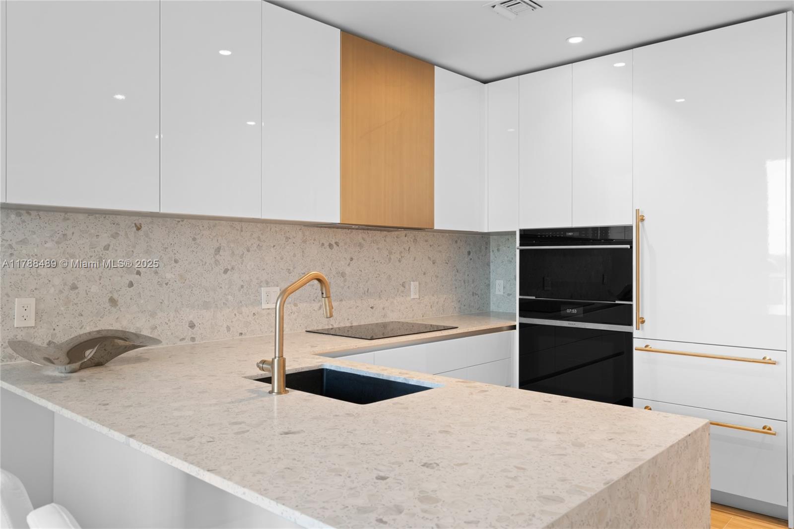 A modern kitchen features white cabinets, a terrazzo backsplash, a gold faucet, and integrated appliances — 2678 Tigertail Ave # 615, Miami FL 33133, MIAMI, FL