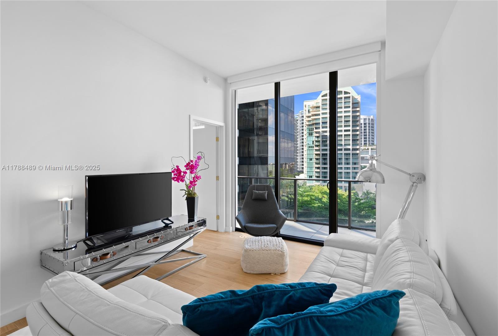 A modern living room features a white sofa, a television, and floor-to-ceiling windows overlooking buildings — 2678 Tigertail Ave # 615, Miami FL 33133, MIAMI, FL