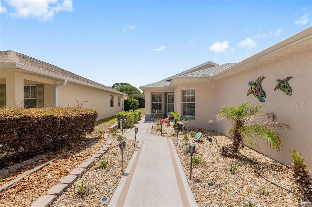A concrete walkway leads to the front entrance of a house with tan stucco siding — 9511 SW 93RD LOOP, OCALA, FL