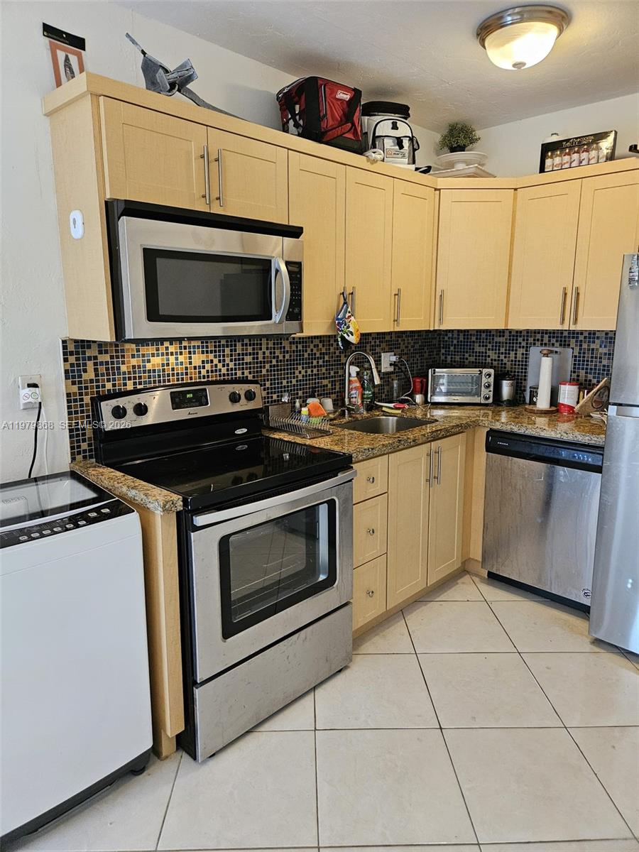 A kitchen features light wood cabinets, stainless steel appliances, and a mosaic tile backsplash — 7400 Harding Ave # 22, Miami Beach FL 33141, MIAMI BEACH, FL