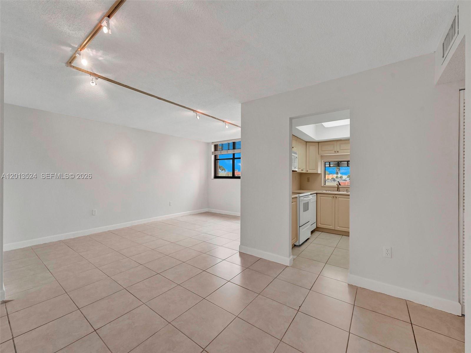 A bright living area with tile flooring and track lighting leads to a small kitchen — 9420 W Flagler St # 312, Miami FL 33174, MIAMI, FL