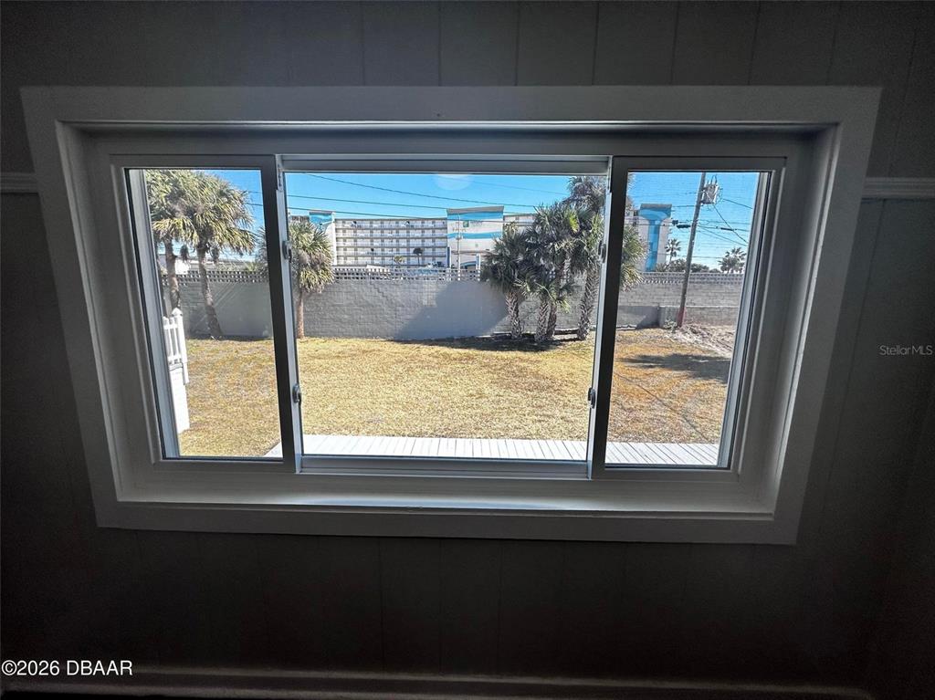 A view of a backyard with palm trees and a large building through a window — 1711 OCEAN DUNES TERRACE, DAYTONA BEACH, FL