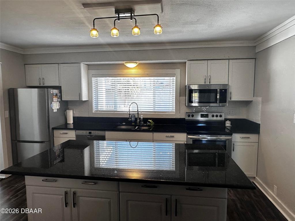 A kitchen features white cabinets, black countertops, a central island, and stainless steel appliances — 1711 OCEAN DUNES TERRACE, DAYTONA BEACH, FL