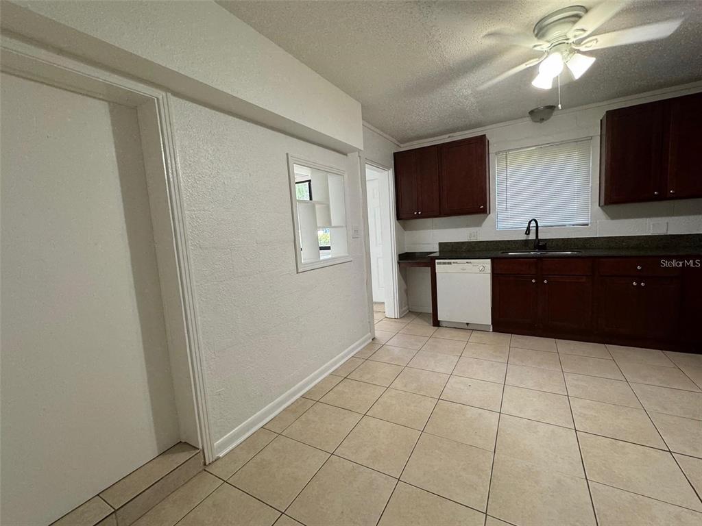 A kitchen features dark wood cabinets, tile flooring, a white dishwasher, and a pass-through window — 2547 S MILLS AVENUE UNIT 2, ORLANDO, FL