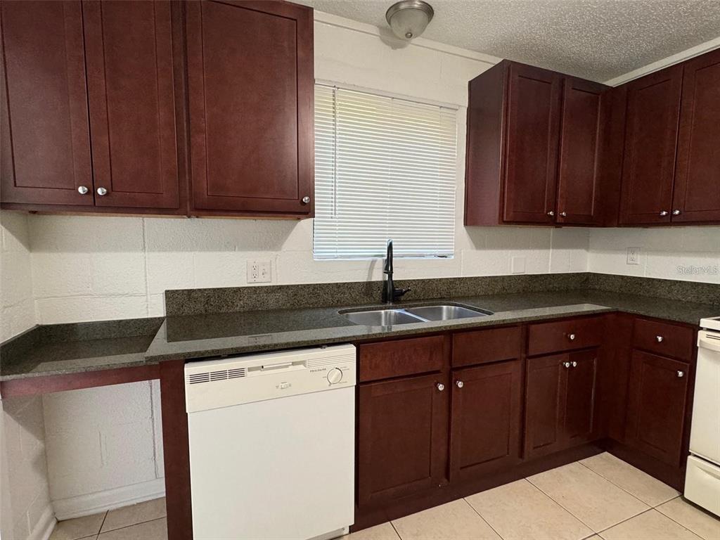A kitchen features dark wood cabinets, a white dishwasher, and a dark granite countertop — 2547 S MILLS AVENUE UNIT 2, ORLANDO, FL
