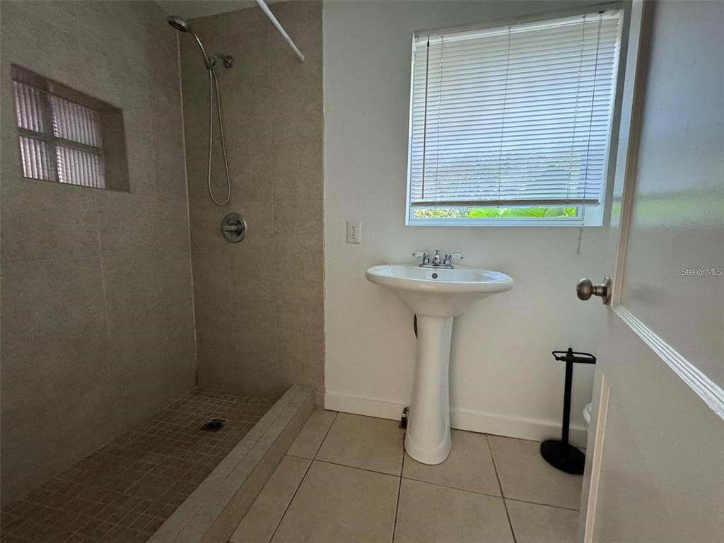 A bathroom features a tiled walk-in shower, a pedestal sink, and a window with blinds — 2547 S MILLS AVENUE UNIT 2, ORLANDO, FL