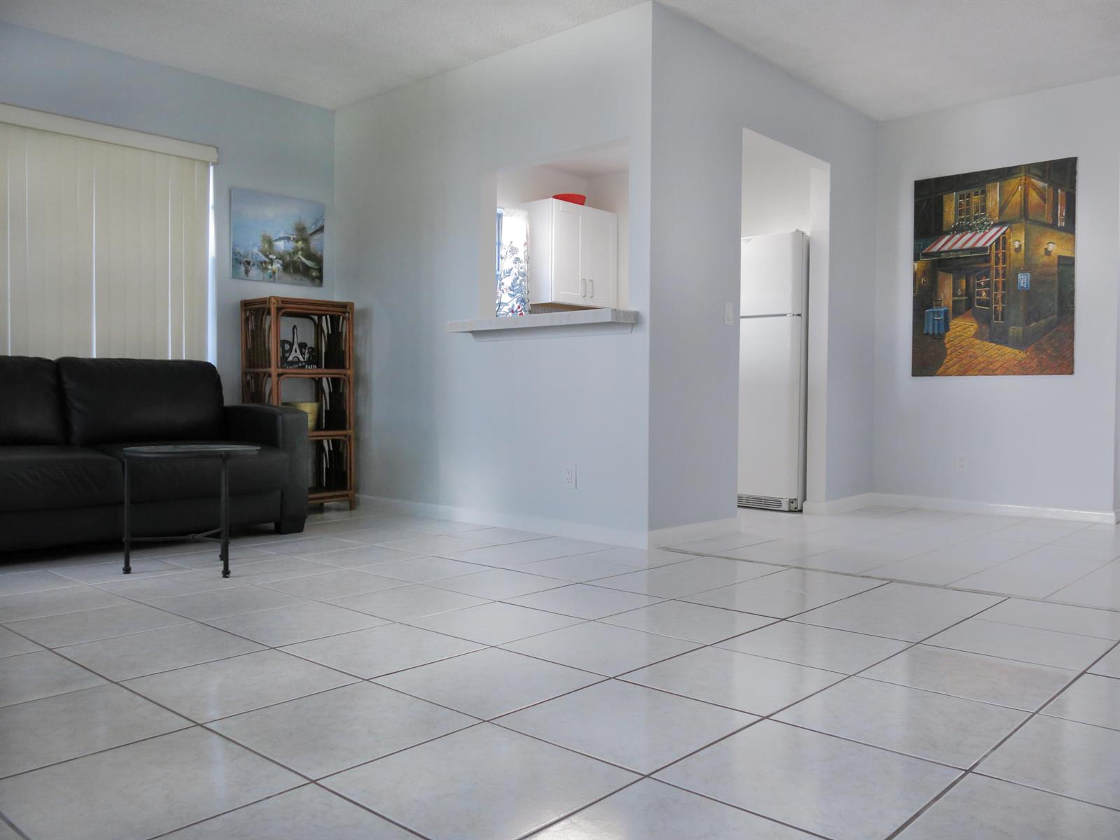 A living room with white tile floors, a black sofa, and a kitchen pass-through window — 331 Windsor O, West Palm Beach FL 33417, WEST PALM BEACH, FL