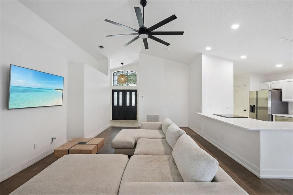 A living room features a large sectional sofa, a wall-mounted television, and dark wood flooring — 2080 CRANBERRY ISLES WAY, APOPKA, FL