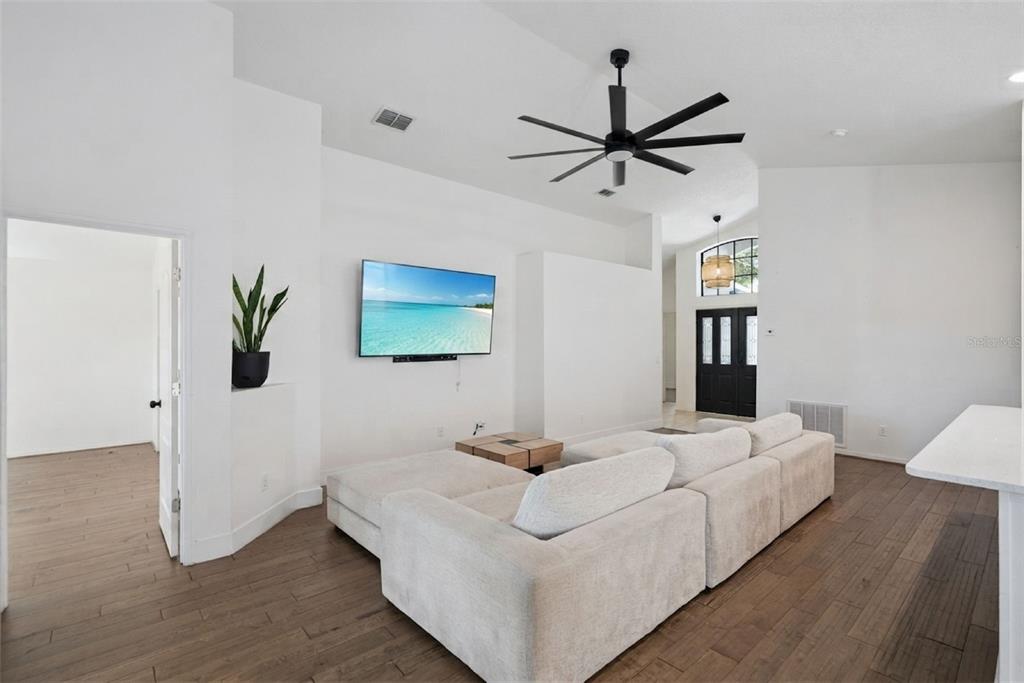 A living room features a white sectional sofa, a wall-mounted television, and wood-look flooring — 2080 CRANBERRY ISLES WAY, APOPKA, FL