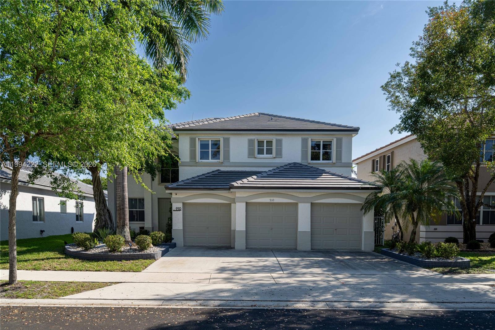 A two-story house with a three-car garage and a light-colored stucco exterior — 910 Sunflower Cir, Weston FL 33327, WESTON, FL