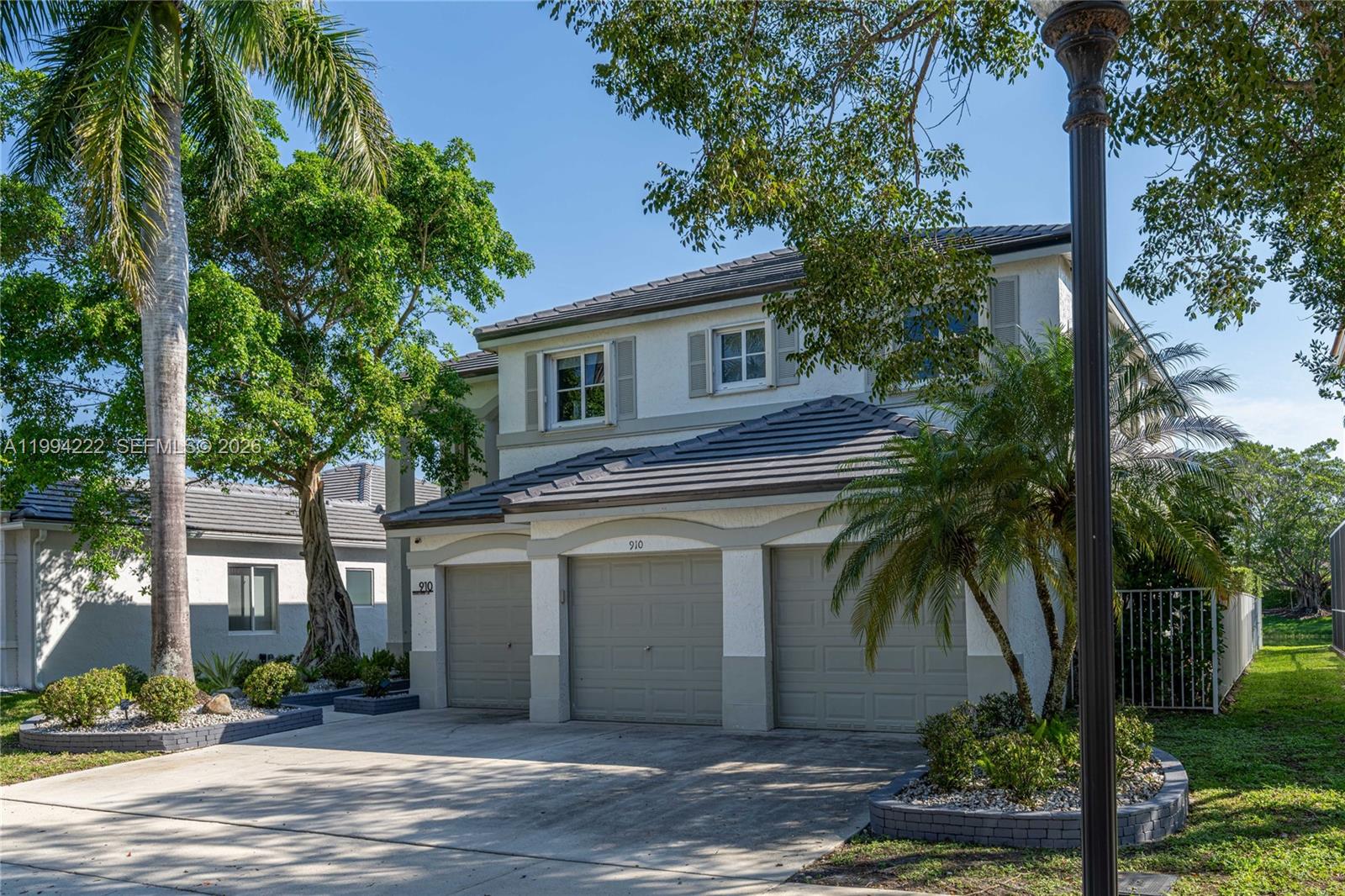A two-story house with a three-car garage and a concrete driveway under a clear sky — 910 Sunflower Cir, Weston FL 33327, WESTON, FL