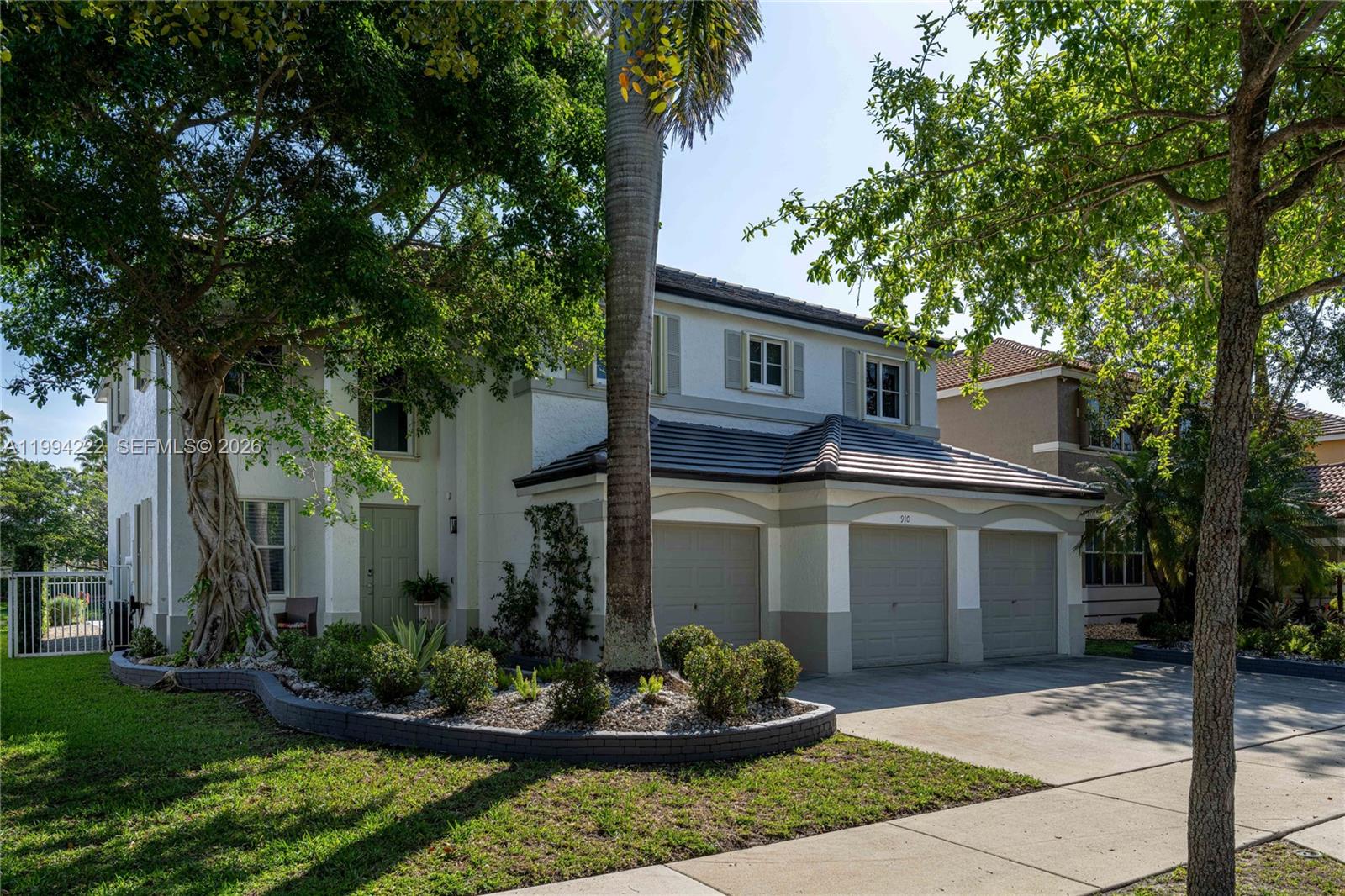 A two-story house with a three-car garage and a landscaped front yard with trees — 910 Sunflower Cir, Weston FL 33327, WESTON, FL