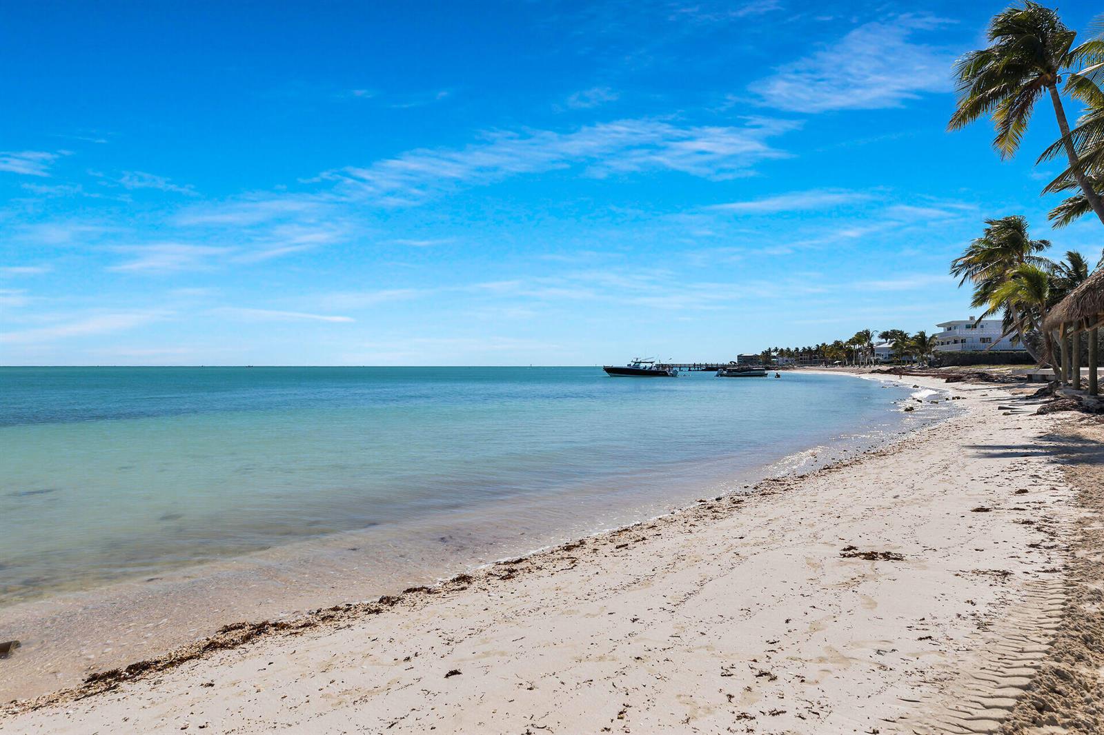 A sandy beach with palm trees, calm water, and boats under a bright blue sky — 601 W Ocean Dr Drive # 203a, FL 33051, FL
