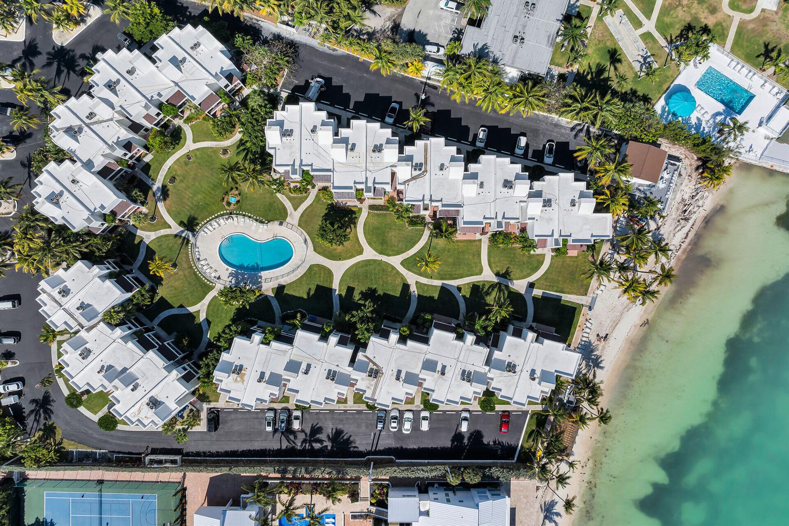 An aerial view shows a beachfront resort complex with white buildings, a pool, and tennis courts — 601 W Ocean Dr Drive # 203a, FL 33051, FL