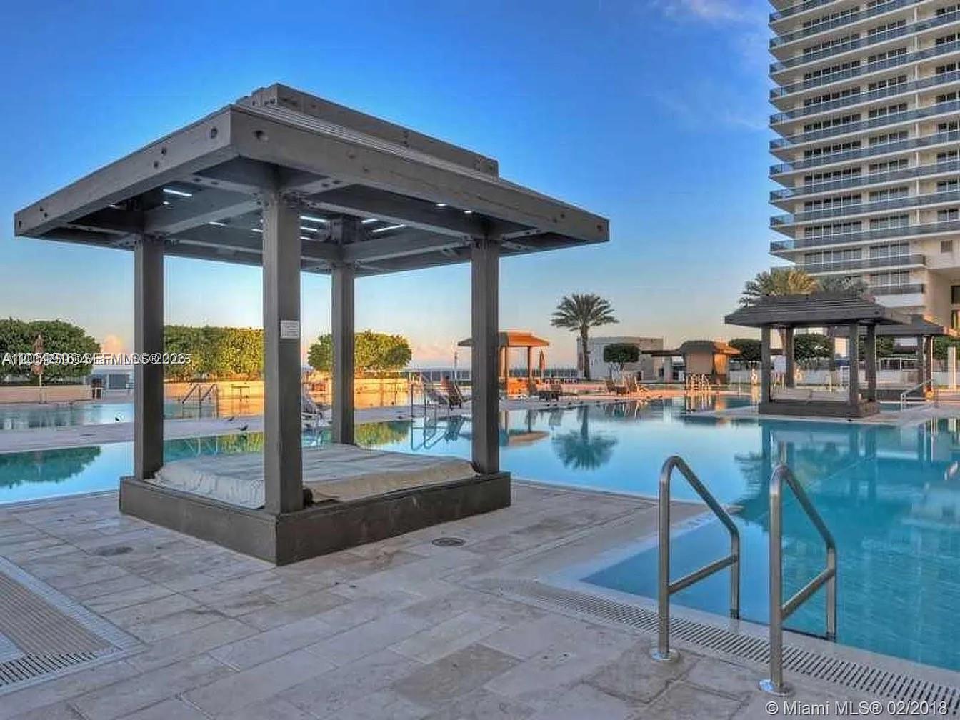 A swimming pool features multiple wooden cabanas on a paved deck beside a high-rise building — 1830 S Ocean Dr # 4007, Hallandale Beach FL 33009, HALLANDALE BEACH, FL