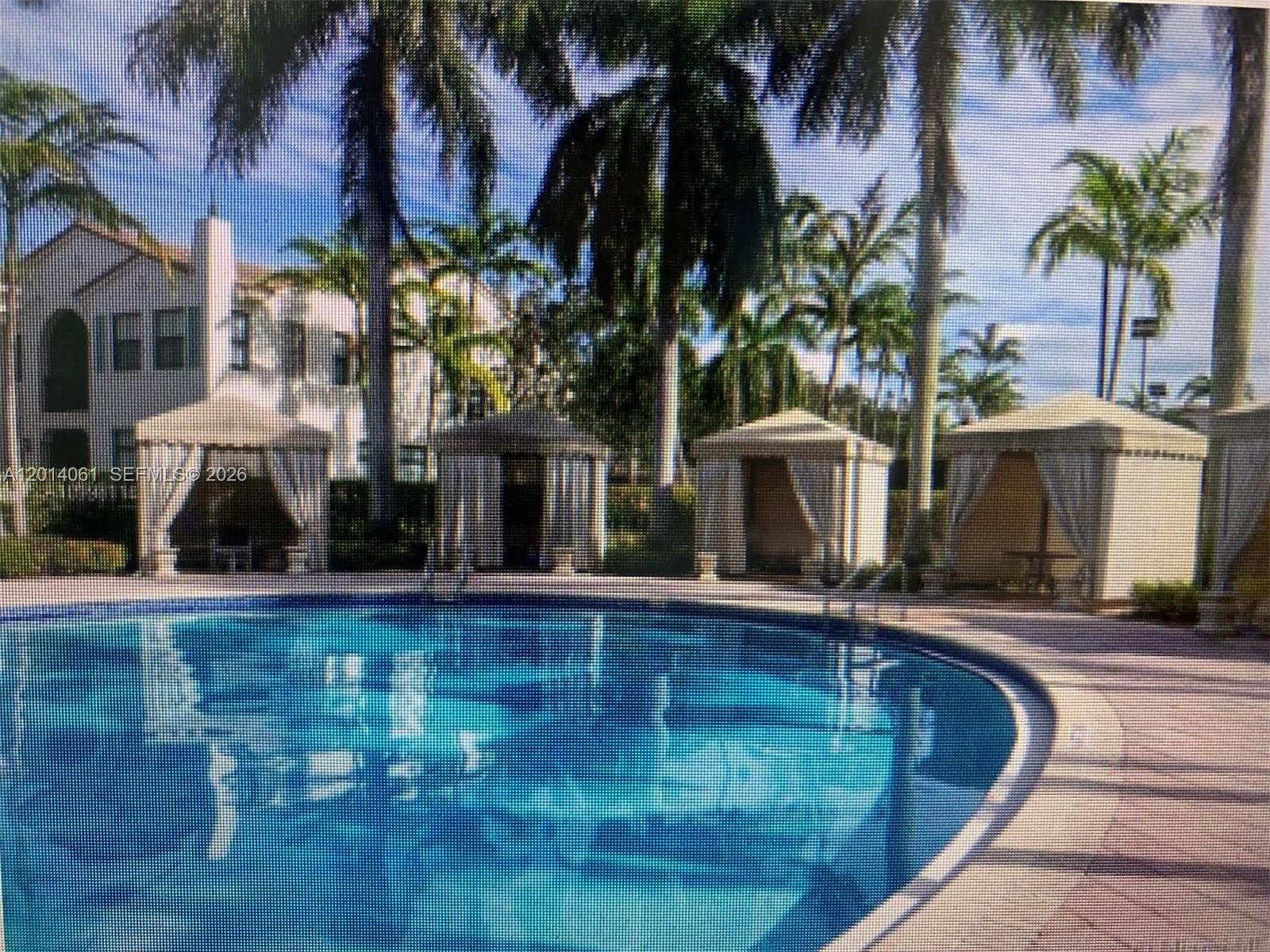 A swimming pool is surrounded by several cabanas and palm trees in front of buildings — 2955 NW 126th Ave # 5, Sunrise FL 33323, SUNRISE, FL