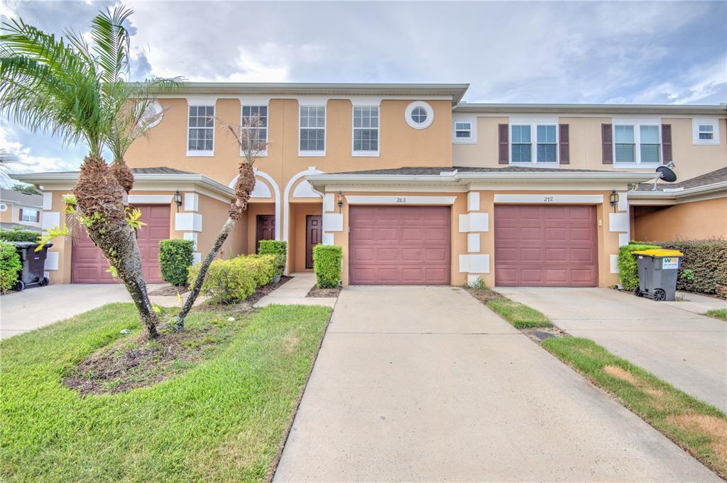 A two-story townhouse exterior features two garage doors, a palm tree, and a driveway — 282 BEXLEY DRIVE, DAVENPORT, FL