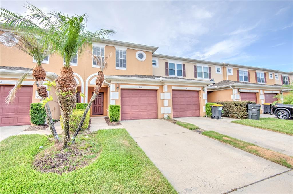 A row of two-story townhouses with tan stucco facades, brown garage doors, and palm trees — 282 BEXLEY DRIVE, DAVENPORT, FL