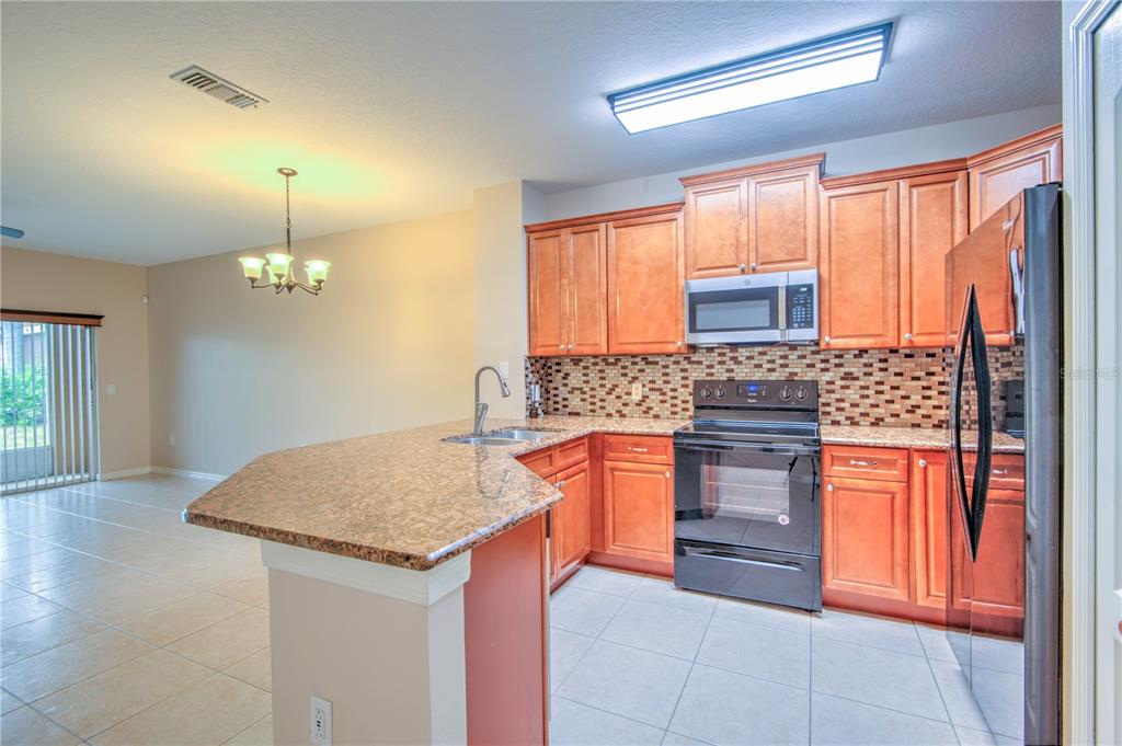 A kitchen features wood cabinets, granite countertops, black appliances, and a tile floor — 282 BEXLEY DRIVE, DAVENPORT, FL