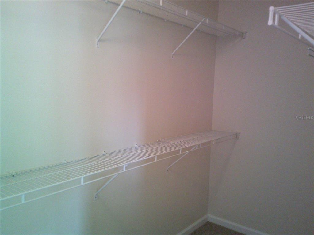 A walk-in closet features white wire shelving mounted on beige walls over carpeted flooring — 6292 TWAIN STREET UNIT 107, ORLANDO, FL