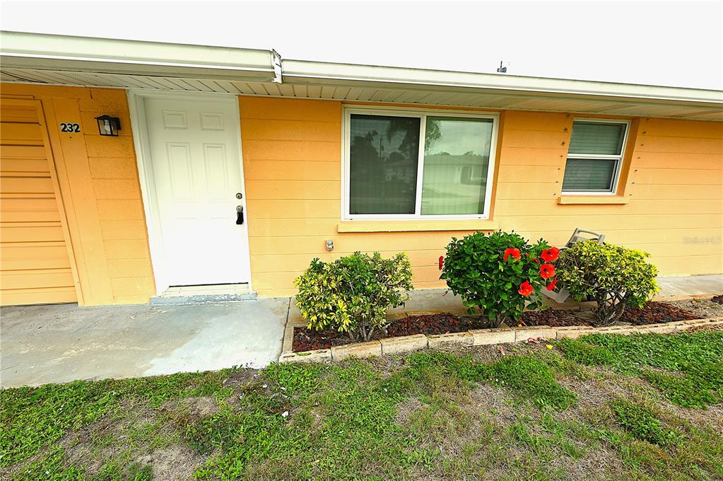A peach-colored exterior wall features a white front door, a window, and small shrubs — 232 SAN MARINO AVENUE, NORTH PORT, FL
