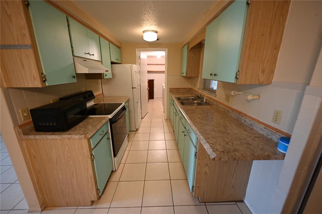 A galley kitchen features light green cabinets, wood-toned lower cabinets, and tan laminate countertops — 232 SAN MARINO AVENUE, NORTH PORT, FL