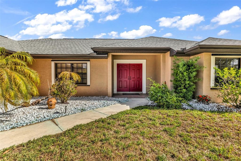A single-story house with a tan exterior, red double front doors, and a stone walkway — 2338 KELSEY COURT, NORTH PORT, FL