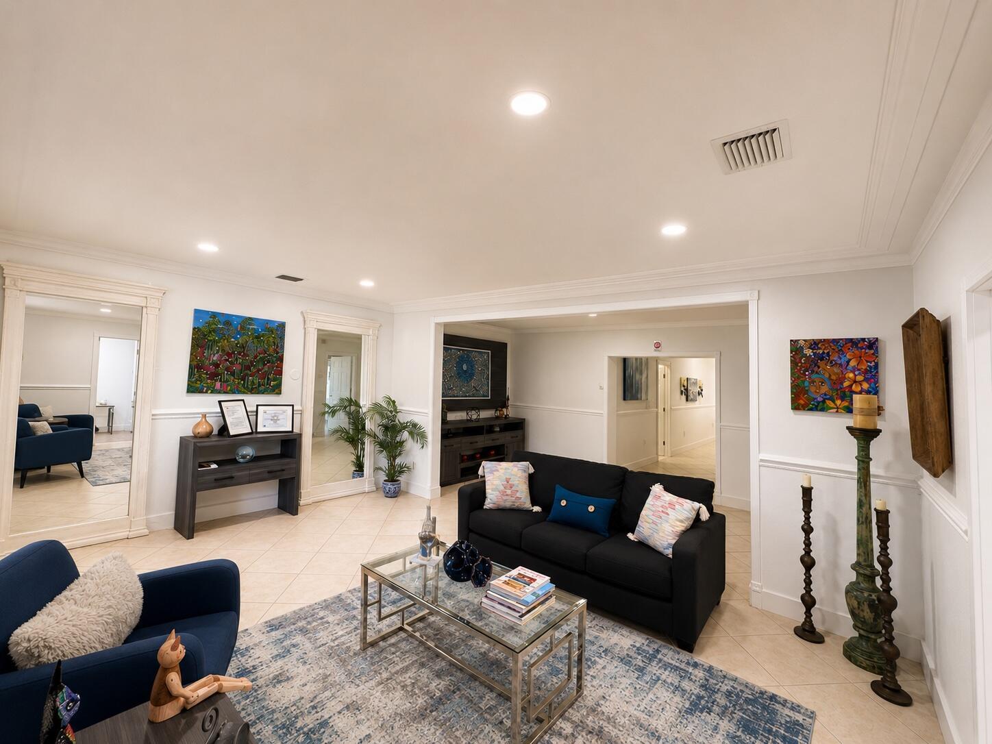 A living room features a black sofa, blue armchair, glass coffee table, and colorful wall art — 150 NE 146th Street NE, Miami FL 33161, MIAMI, FL