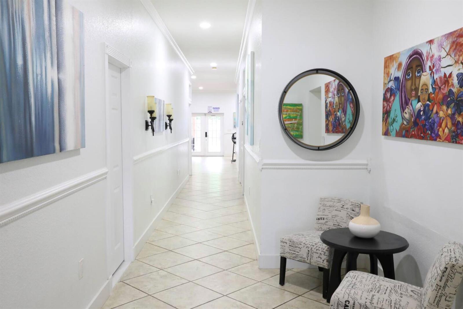 A bright hallway features white walls, tile flooring, a round mirror, and two patterned chairs — 150 NE 146th Street NE, Miami FL 33161, MIAMI, FL