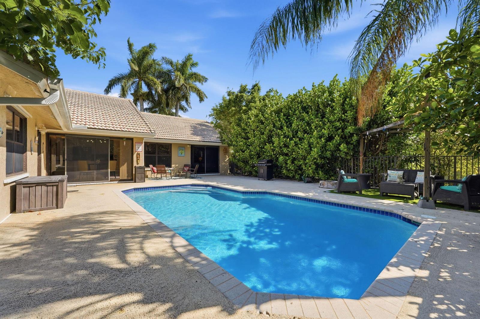 A backyard features a swimming pool, a patio, outdoor furniture, and lush green landscaping — 9577 Majestic Way, Boynton Beach FL 33437, BOYNTON BEACH, FL