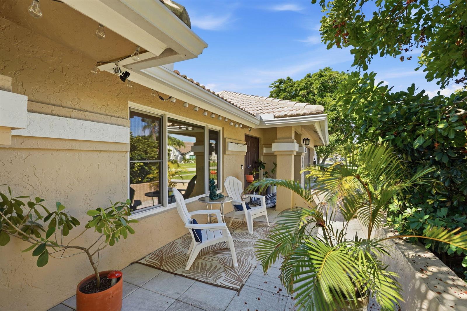 A beige stucco house features a covered patio with white chairs and potted plants — 9577 Majestic Way, Boynton Beach FL 33437, BOYNTON BEACH, FL