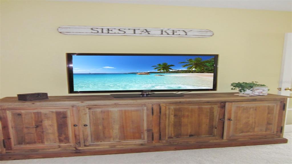 A television sits on a wooden media console below a Siesta Key wall sign — 1344 SIESTA BAYSIDE DRIVE UNIT 1344-D, SARASOTA, FL
