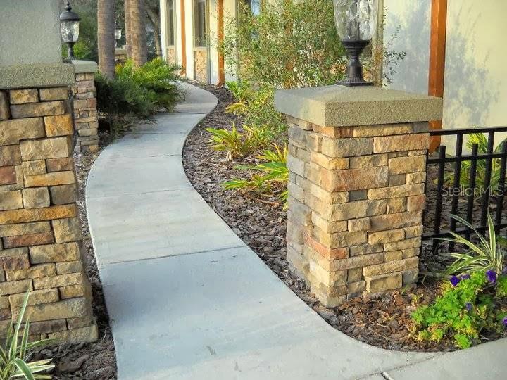A concrete walkway curves past stone pillars and landscaping toward the entrance of a building — 3632 LAND O LAKES BOULEVARD UNIT 104-3, LAND O LAKES, FL