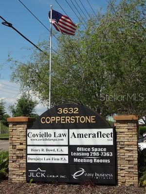 A stone monument sign displays business names and office leasing information under an American flag — 3632 LAND O LAKES BOULEVARD UNIT 104-3, LAND O LAKES, FL