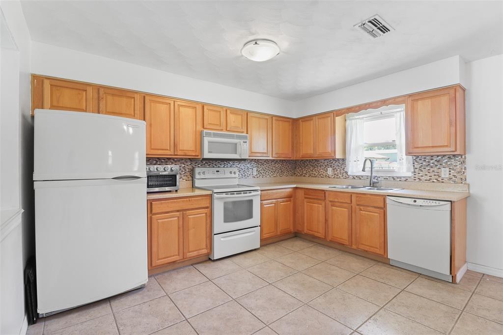 A kitchen with light wood cabinets, white appliances, a tiled backsplash, and beige floor tiles — 1509 WYOMING AVENUE, ST CLOUD, FL