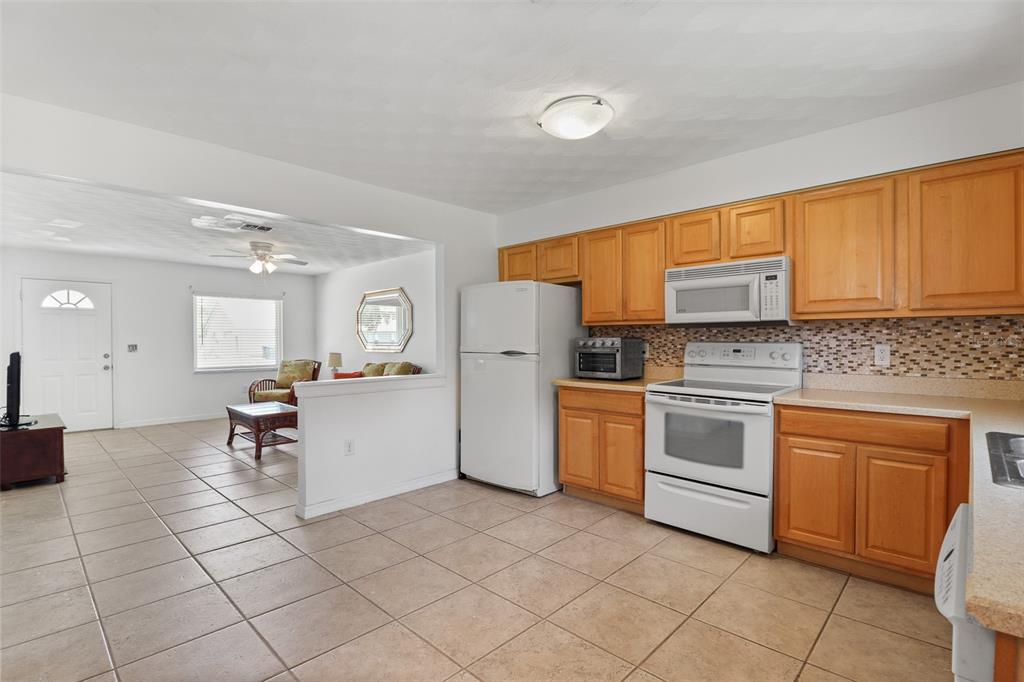 A kitchen with light wood cabinets and white appliances opens into a living area — 1509 WYOMING AVENUE, ST CLOUD, FL