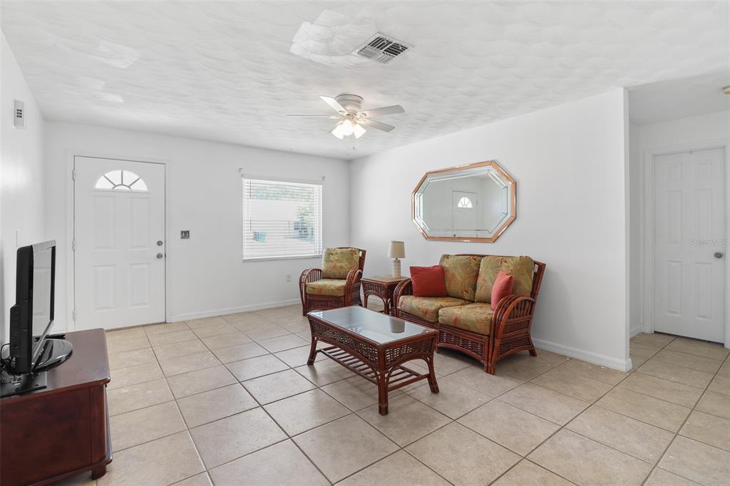 A living room features white walls, tile flooring, a ceiling fan, and wicker-style furniture — 1509 WYOMING AVENUE, ST CLOUD, FL