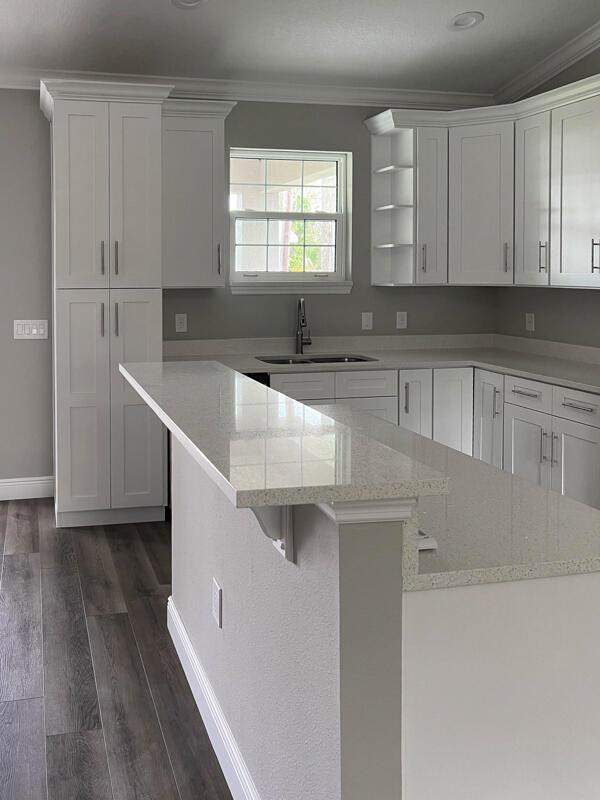 A kitchen features white shaker cabinets, quartz countertops, and gray wood-look flooring — 528 SE 35th Terrace, Okeechobee FL 34974, OKEECHOBEE, FL