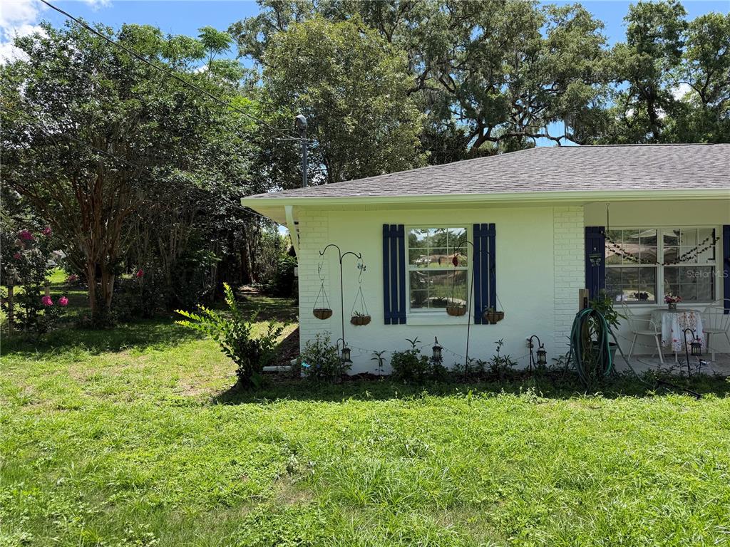 A side view of a white brick house with blue shutters and hanging planters — 12315 SE 60TH TERRACE, BELLEVIEW, FL