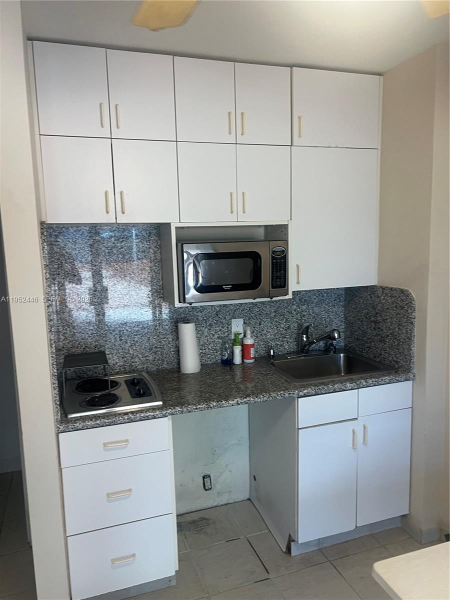 A small kitchen features white cabinets, granite countertops, a stainless steel sink, and a microwave — 9801 Collins Ave, Bal Harbour FL 33154, BAL HARBOUR, FL