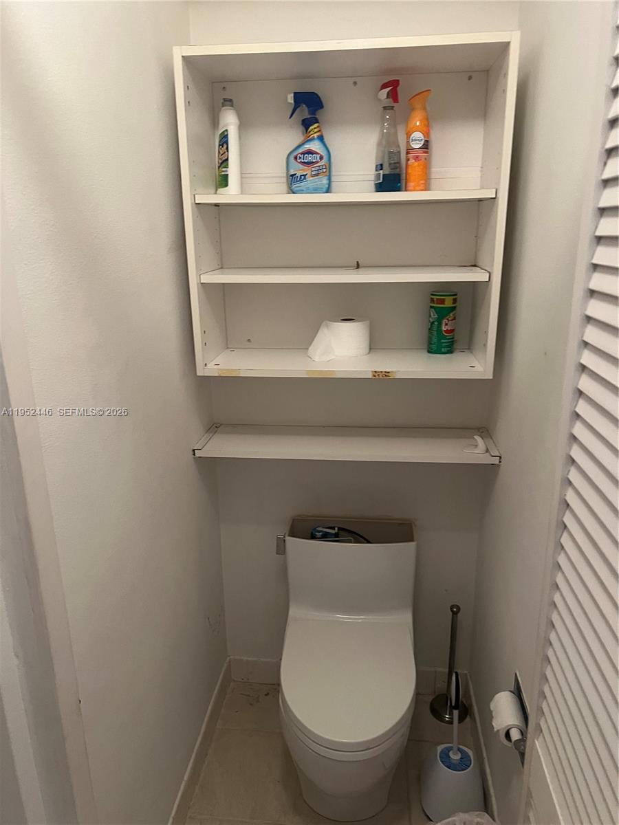 A white toilet is positioned beneath a wall-mounted storage unit with open shelving — 9801 Collins Ave, Bal Harbour FL 33154, BAL HARBOUR, FL
