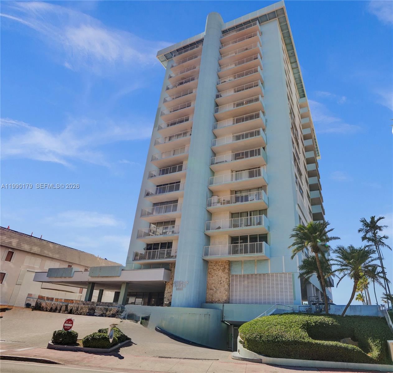 A tall, light blue residential high-rise building stands under a clear blue sky — 5838 Collins Ave # 7G, Miami Beach FL 33140, MIAMI BEACH, FL