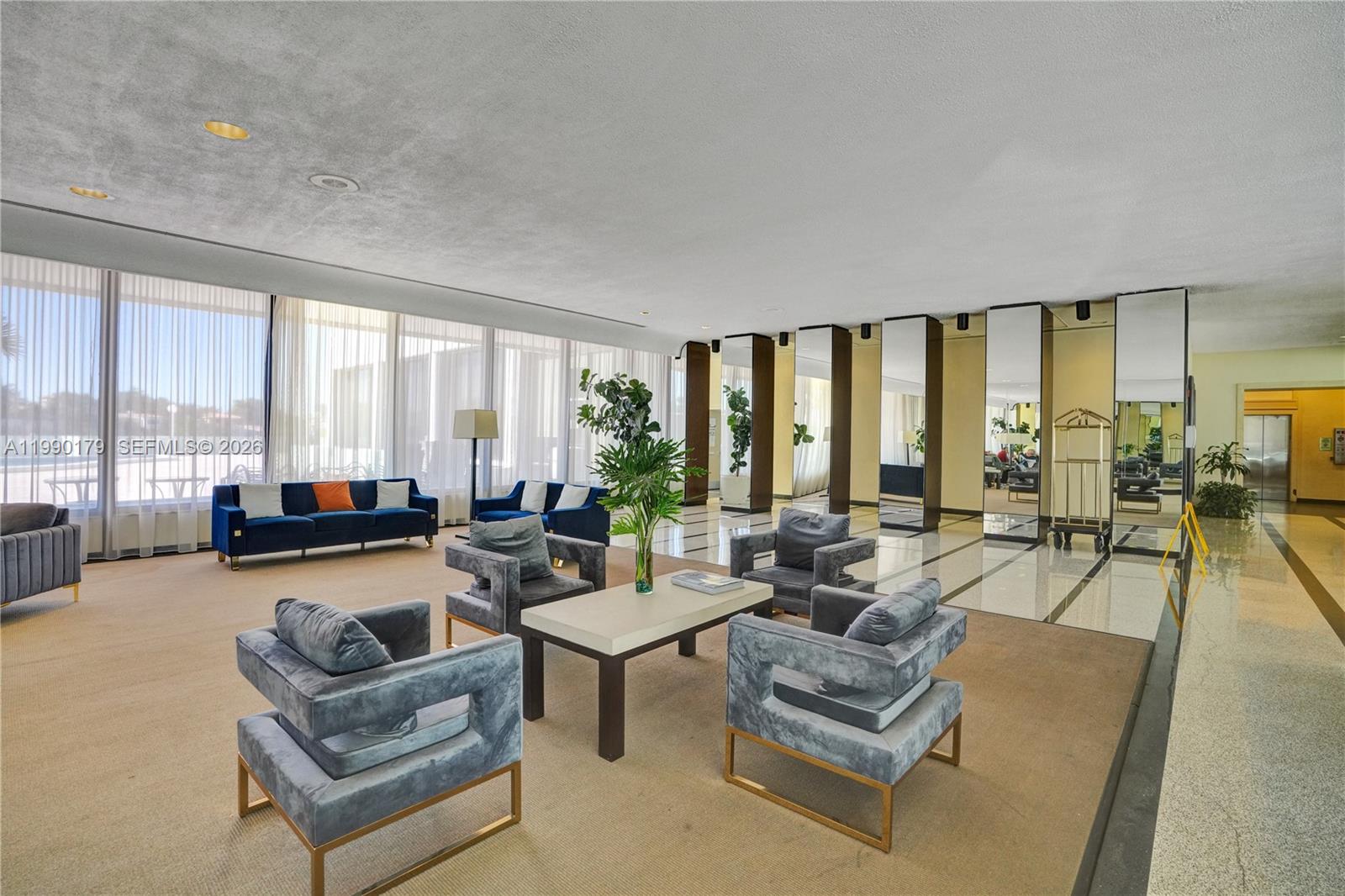 A spacious lobby features blue velvet seating, a central coffee table, and floor-to-ceiling windows — 5838 Collins Ave # 7G, Miami Beach FL 33140, MIAMI BEACH, FL