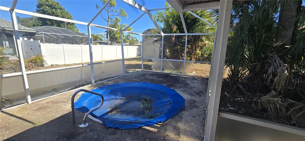 A screened-in patio features a small, circular pool covered by a blue tarp — 2094 CARPETGREEN STREET, PORT CHARLOTTE, FL