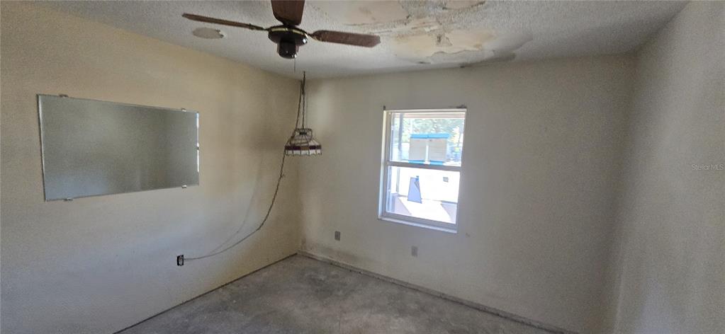An empty room features a ceiling fan, a hanging light fixture, and a wall mirror — 2094 CARPETGREEN STREET, PORT CHARLOTTE, FL