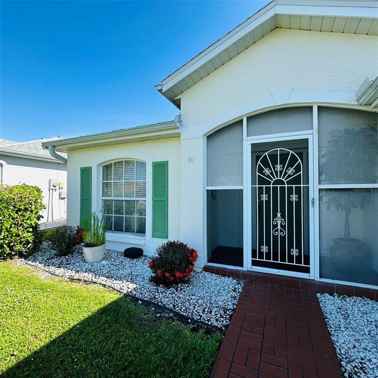 A single-story house exterior features a white stucco facade, green shutters, and a screened entryway — 13412 SW PEMBROKE CIRCLE N, LAKE SUZY, FL
