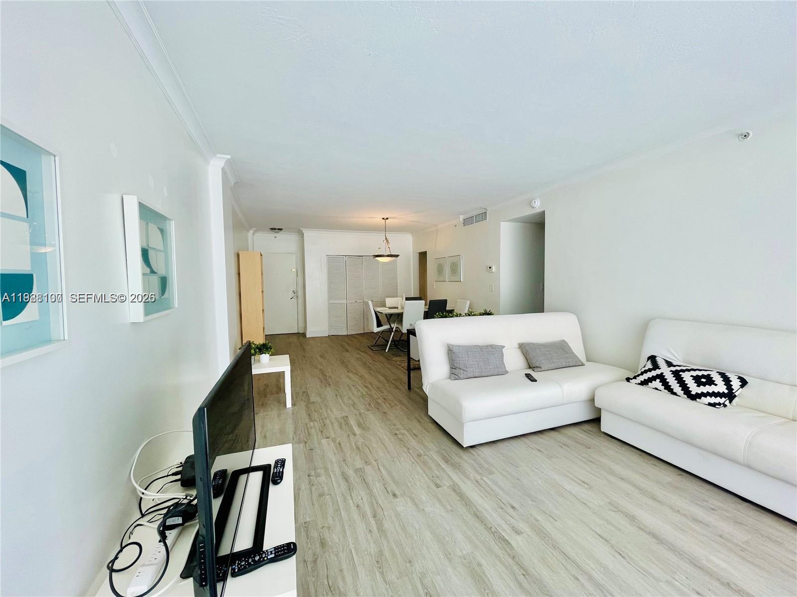 A living room with light wood-look flooring, white walls, and two white sofas — 3001 S Ocean Dr # 101, Hollywood FL 33019, HOLLYWOOD, FL